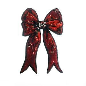 May include: A red sequined bow with a black outline and pearl accents. The bow is a decorative embellishment for clothing or crafts.
