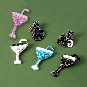 Może przedstawiać: Zestaw sześciu naszywek do prasowania z koralikami i haftem, przedstawiających różne wzory, w tym kieliszek do koktajlu, butelkę i gwiazdę. Naszywki są w kolorze czarnym, białym i niebieskim.