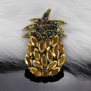 Può includere: Una spilla a forma di ananas in strass dorati e verdi. L'ananas è realizzata in strass dorati e le foglie sono realizzate in strass verdi.