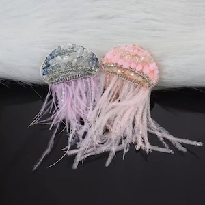 May include: Two pink and blue jeweled jellyfish brooches with pink feather accents.