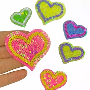 May include: Six heart-shaped patches with sequin embellishments. The patches are in various colors, including pink, yellow, green, and blue.
