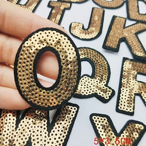 Könnte beinhalten: Goldene Buchstaben-Patches mit schwarzem Filzrücken. Die Buchstaben sind O, Q, R, W und V. Jeder Buchstabe ist etwa 5 Zoll mal 3,5 Zoll groß.