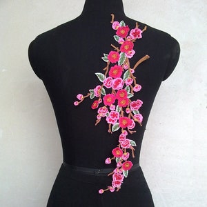 May include: Pink and green embroidered floral applique with a delicate branch design. This floral applique is perfect for adding a touch of elegance to clothing, bags, or home decor projects.