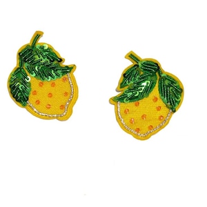 May include: Two yellow embroidered strawberry patches with green sequined leaves and orange dot details. The strawberries have a silver border and are set against a white background. These patches are ideal for adding a decorative touch to clothing or accessories.