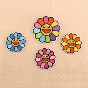 May include: Four embroidered iron-on patches featuring smiling flower faces with different coloured petals. The flowers are blue, pink, yellow, and rainbow.