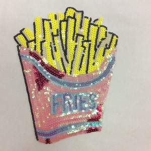 Könnte beinhalten: Ein Pailletten-Patch in Form eines Pommes-Frites-Behälters. Der Behälter ist rosa mit blauen und irisierenden Pailletten. Das Wort "FRIES" ist in blauen Pailletten geschrieben. Die Pommes sind gelb mit schwarzen Umrissen.
