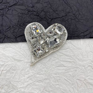 May include: A white heart-shaped patch with a design of clear rhinestones in various shapes and sizes.