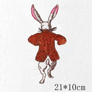 Puede incluir: Parche bordado con un conejo con una chaqueta roja, visto por detrás. El conejo tiene orejas largas con el interior rosa. El parche mide 21 cm por 10 cm.