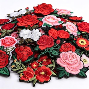 May include: A collection of embroidered fabric patches featuring various floral designs, including red, pink, and white roses with green leaves. The patches are layered together, showcasing detailed stitching and vibrant thread colors in a dense arrangement.