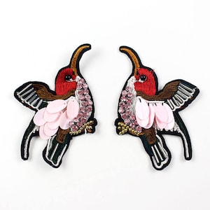 May include: Two embroidered hummingbird patches with pink sequins, rhinestones, and gold beads. The hummingbirds are facing opposite directions.