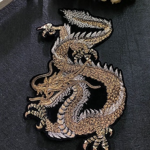 May include: A gold and silver embroidered dragon applique patch on a black velvet background. The dragon is curled up with its tail in its mouth.