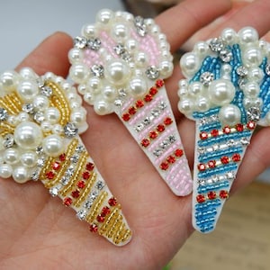 May include: Three beaded ice cream cone patches. Each patch features a cone shape with red, gold, or blue accents, topped with faux pearls and rhinestones. The ice cream scoops are adorned with white pearls and rhinestones.