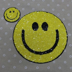 May include: Two yellow smiley face iron-on patches with black outlines. The larger patch is made of sequins.