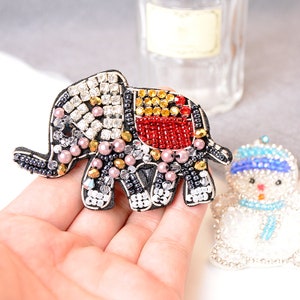May include: A beaded elephant and snowman applique patch. The elephant is black, white, red, gold, and pink. The snowman is white, blue, and silver.