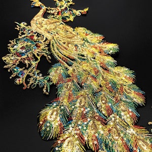 May include: Gold, green, and blue sequined peacock applique with a floral design. The peacock has a long tail with iridescent feathers.