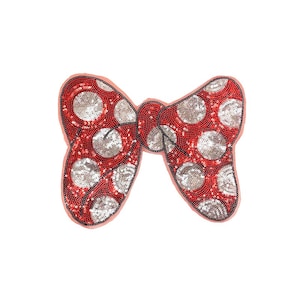 Puede incluir: Un lazo rojo y plateado con lentejuelas y lunares blancos. El lazo es un adorno decorativo para la ropa o la artesanía.