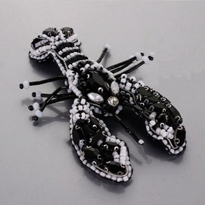 May include: A black and white beaded lobster brooch with a rhinestone accent. The lobster is detailed with black and white beads and has a shiny black finish.