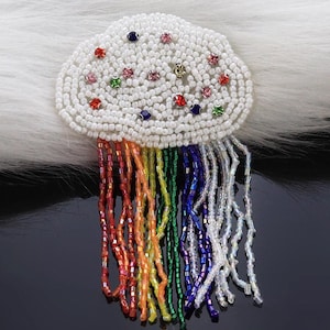 May include: A beaded cloud-shaped brooch with a rainbow of dangling beads. The cloud is white with colorful gems, and the beaded strands cascade in red, orange, yellow, green, blue, and white. This accessory is perfect for adding a touch of whimsy.