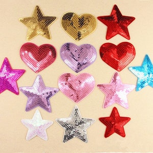 May include: A selection of sequined star and heart-shaped patches in a range of colours. The patches include gold, red, pink, purple, silver, and blue. These decorative embellishments are suitable for adding flair to clothing or crafts.