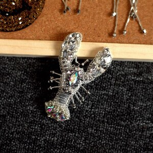 May include: A silver and iridescent beaded lobster brooch with a large, clear rhinestone in the centre.