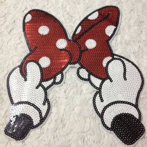 Puede incluir: Lazo rojo y blanco de lentejuelas con guantes blancos de lentejuelas. El lazo tiene lunares blancos y los guantes tienen contornos negros.