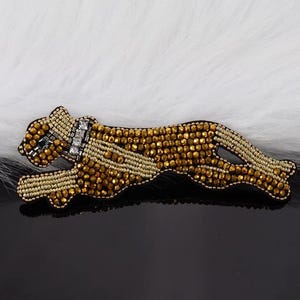 May include: A gold and brown beaded leopard applique with rhinestones. The applique is on a white fluffy background.
