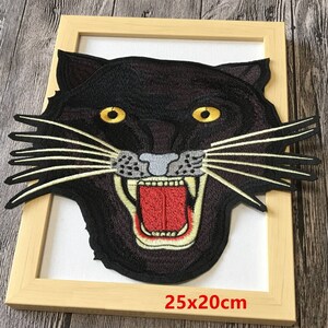 Puede incluir: Parche bordado negro de cabeza de pantera con una expresión feroz, ojos amarillos y lengua roja. El parche mide 25x20cm.