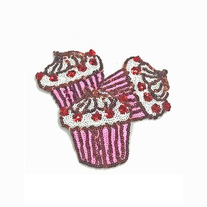 Puede incluir: Tres cupcakes de lentejuelas rosas y marrones con glaseado blanco y cerezas rojas. Los cupcakes están apilados uno encima del otro.