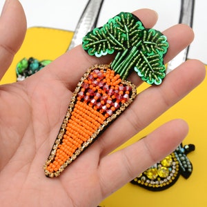 Puede incluir: Una aplicación de zanahoria bordada con hojas de lentejuelas verdes. La zanahoria es naranja y roja con detalles dorados.