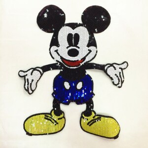 May include: A sequined Mickey Mouse patch. The character has black ears, arms, and legs, a white face and hands, a red mouth, and blue shorts. The shoes are yellow.