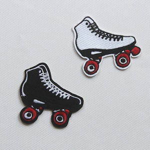 Op de afbeelding: Twee geborduurde strijkbare patches van rol schaatsen. Eén is zwart met witte stiksels en de andere is wit met zwarte stiksels. Beide hebben rode wielen.