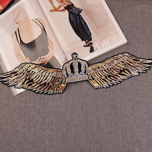 May include: Gold and silver sequined wings with a gold crown in the center. The wings are spread out and the crown is facing forward.