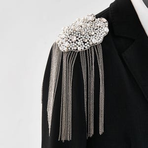 May include: A black blazer with a pearl and chain embellishment on the shoulder.