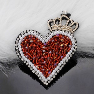 May include: A red beaded heart with a gold crown on top. The heart is surrounded by white pearls and the crown has clear rhinestones.