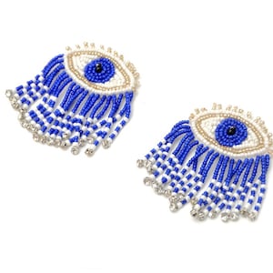 Op de afbeelding: Een paar blauwe en witte kralen oorbellen met een blauwe kwade oog charme. De oorbellen hebben een franje van kralen en strass.