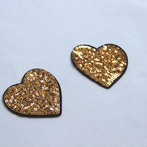 May include: Two gold heart-shaped patches with sequins. The hearts are outlined in black.