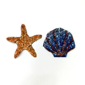 May include: Two sparkly fabric patches, one a gold starfish and the other a blue seashell with orange stripes.