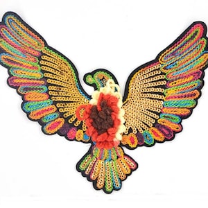 May include: A colorful embroidered patch of a bird with outstretched wings. The bird is made of sequins and yarn, with a red, brown, and yellow flower in the center.
