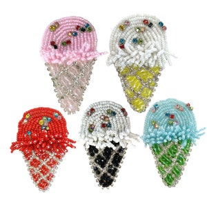 May include: Five beaded ice cream cone ornaments in different colours. The cones are made of clear beads with a diamond pattern. The ice cream is made of white beads with colourful sprinkles. The colours of the ice cream are pink, white, red, white, and blue.