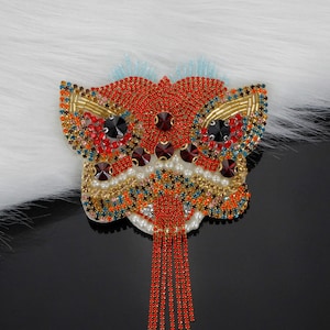 May include: A red, gold, and blue beaded lion dance mask with a long red beaded tassel. The mask is decorated with rhinestones and pearls.