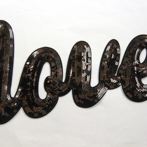 Könnte beinhalten: Ein schwarzer und brauner Pailletten-Patch mit der Aufschrift "love" in kursiver Schrift.