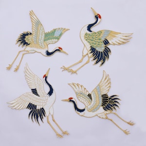 May include: Four embroidered crane patches featuring white, black, and gold thread with accents of light blue and green. Each crane is depicted in a different flying pose with outstretched wings, long necks, and red markings on their heads.