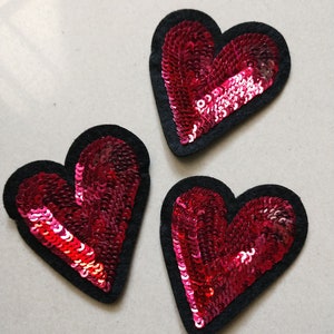 May include: Three red heart-shaped patches with black felt backing and sequins.