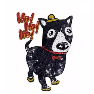 Op de afbeelding: Een zwart pailletten hondenpatch met een witte snuit, met een gele hoed en een rode vlinderdas. De patch heeft de tekst "Hey Ho! Ho!" in rode pailletten. De hond staat op zijn achterpoten.