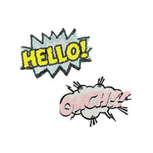 Può includere: Due toppe termoadesive colorate con un design a fumetto. La prima toppa dice "HELLO!" in lettere gialle su sfondo blu. La seconda toppa dice "OUCH!" in lettere rosa su sfondo bianco.