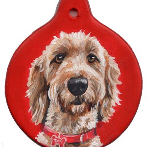 May include: A hand-painted ornament featuring a portrait of a brown and white dog with a red collar and a bone-shaped tag that says "Teddy". The ornament is round and has a red background.