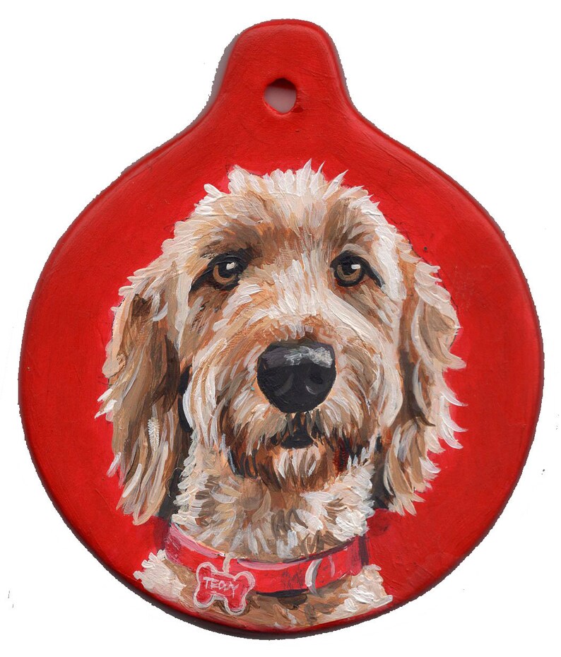May include: A hand-painted ornament featuring a portrait of a brown and white dog with a red collar and a bone-shaped tag that says "Teddy". The ornament is round and has a red background.