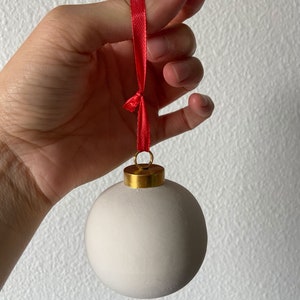 May include: A white ceramic Christmas ornament with a gold top and a red ribbon.