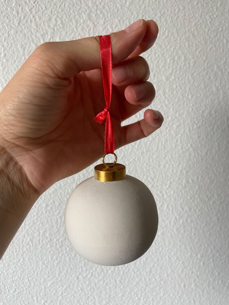 May include: A white ceramic Christmas ornament with a gold top and a red ribbon.