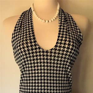 May include: A black and white houndstooth halter top with a white beaded necklace.